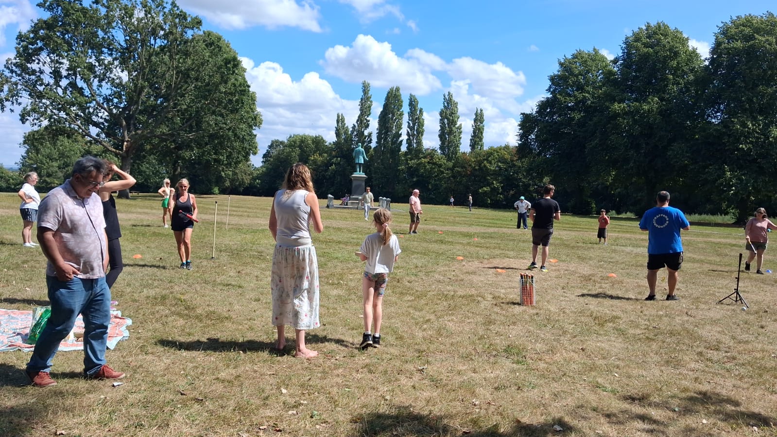 Residents playing rounders on the open lawn of Verdin Park, with the park statue and mature trees in the background