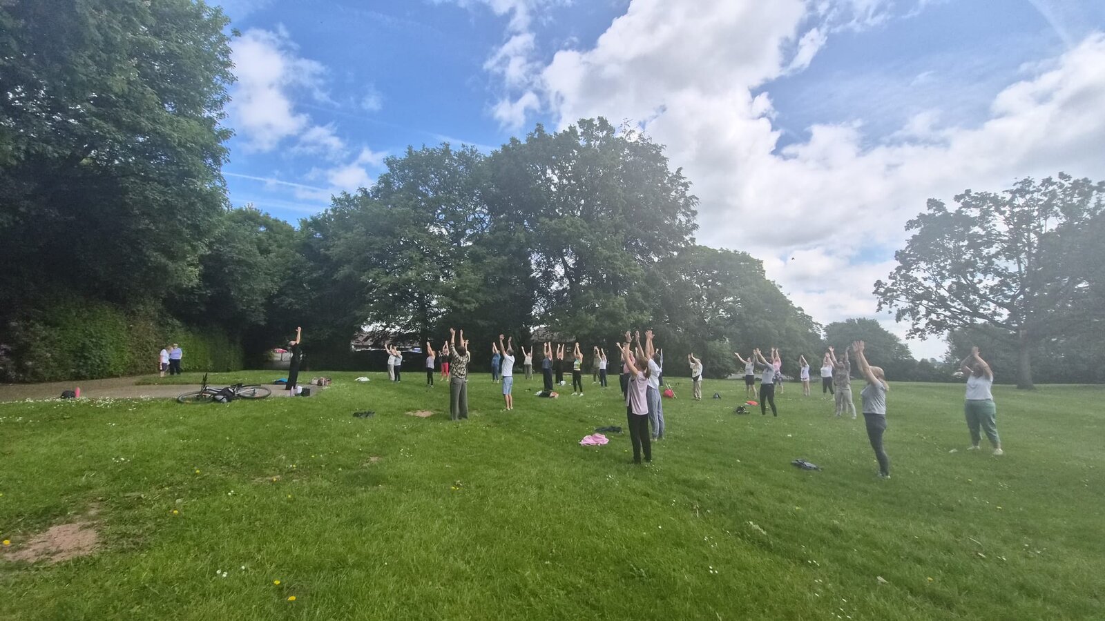 Tai Chi participants with arms raised against a blue sky in Verdin Park